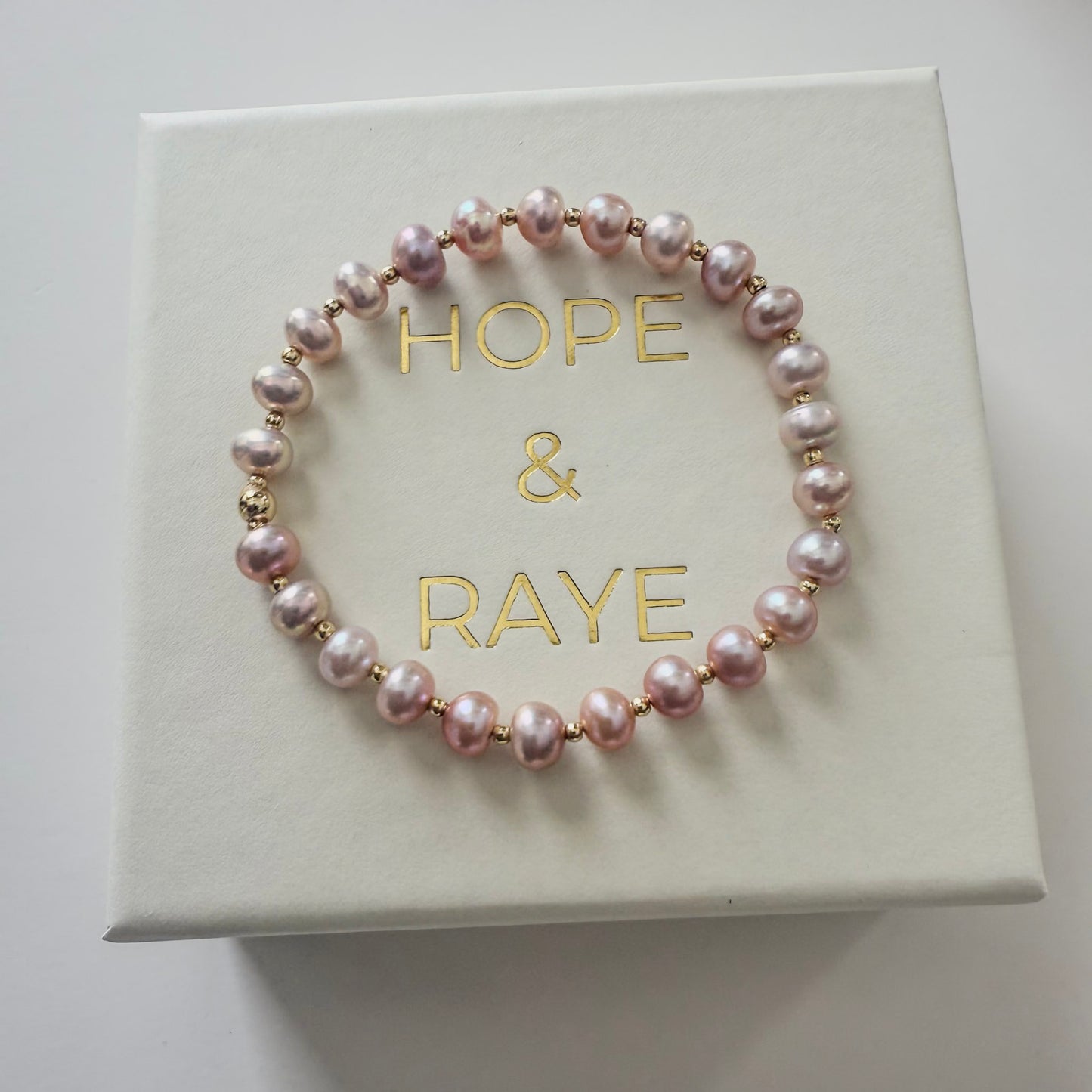 Pink pearl bracelet with gold placed on jewelry box included in all jewelry shipments from HOPE & RAYE.