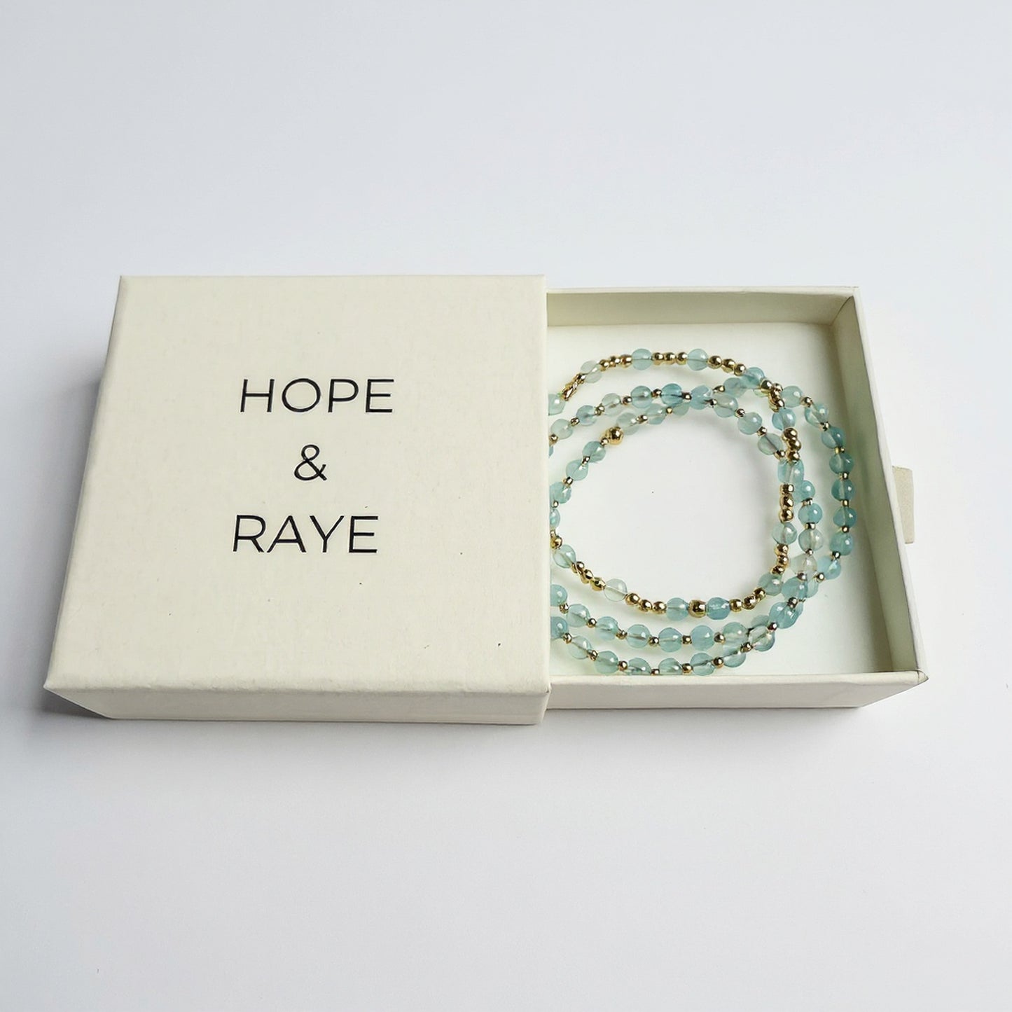 Aquamarine beaded bracelet stack of three with gold beads in Hope & Raye branded jewelry box.