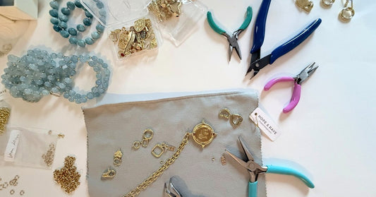 Handmade jewelry workspace featuring aquamarine gemstone bracelets, 18K gold-filled chains, charms, and artisan tools on a HOPE & RAYE jewelry pouch