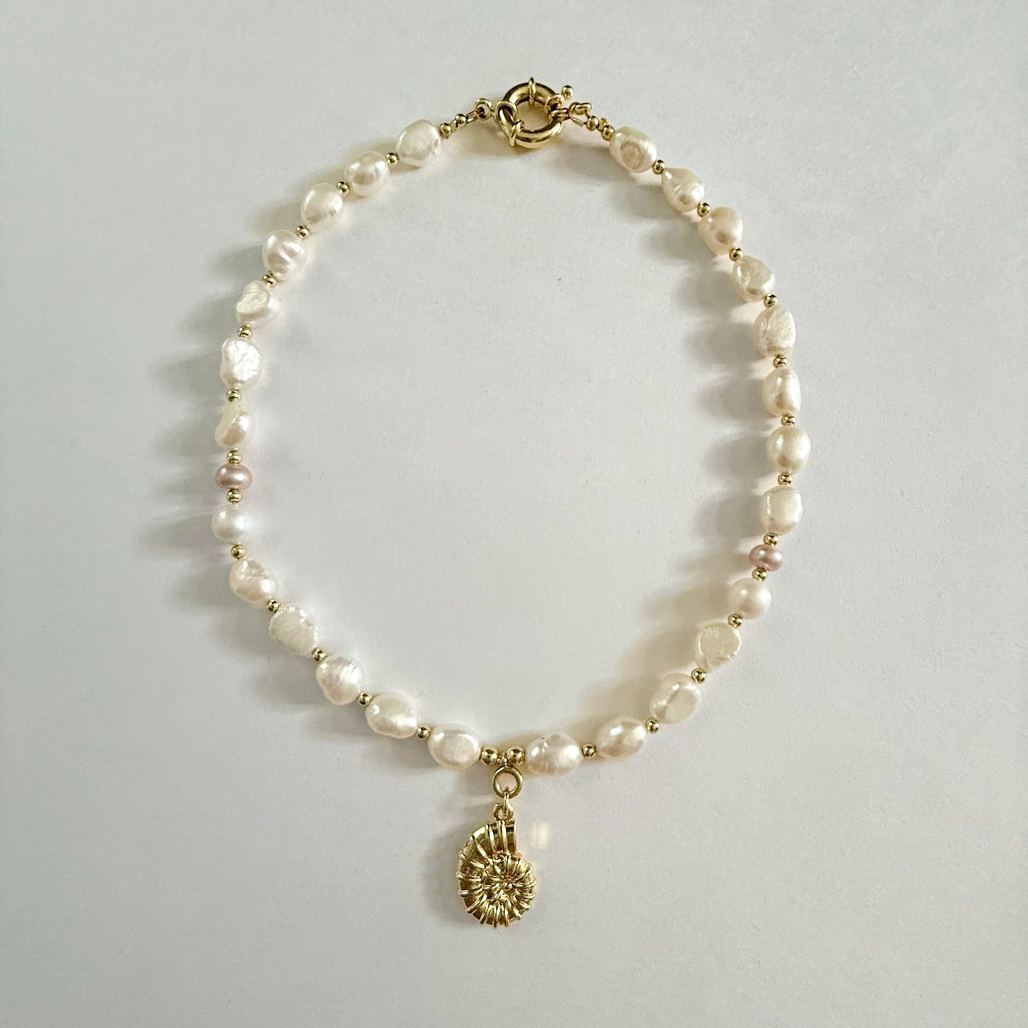 Baroque pearl necklace with two pink round pearl accents, gold spring clasp, and gold shell charm by Hope and Raye