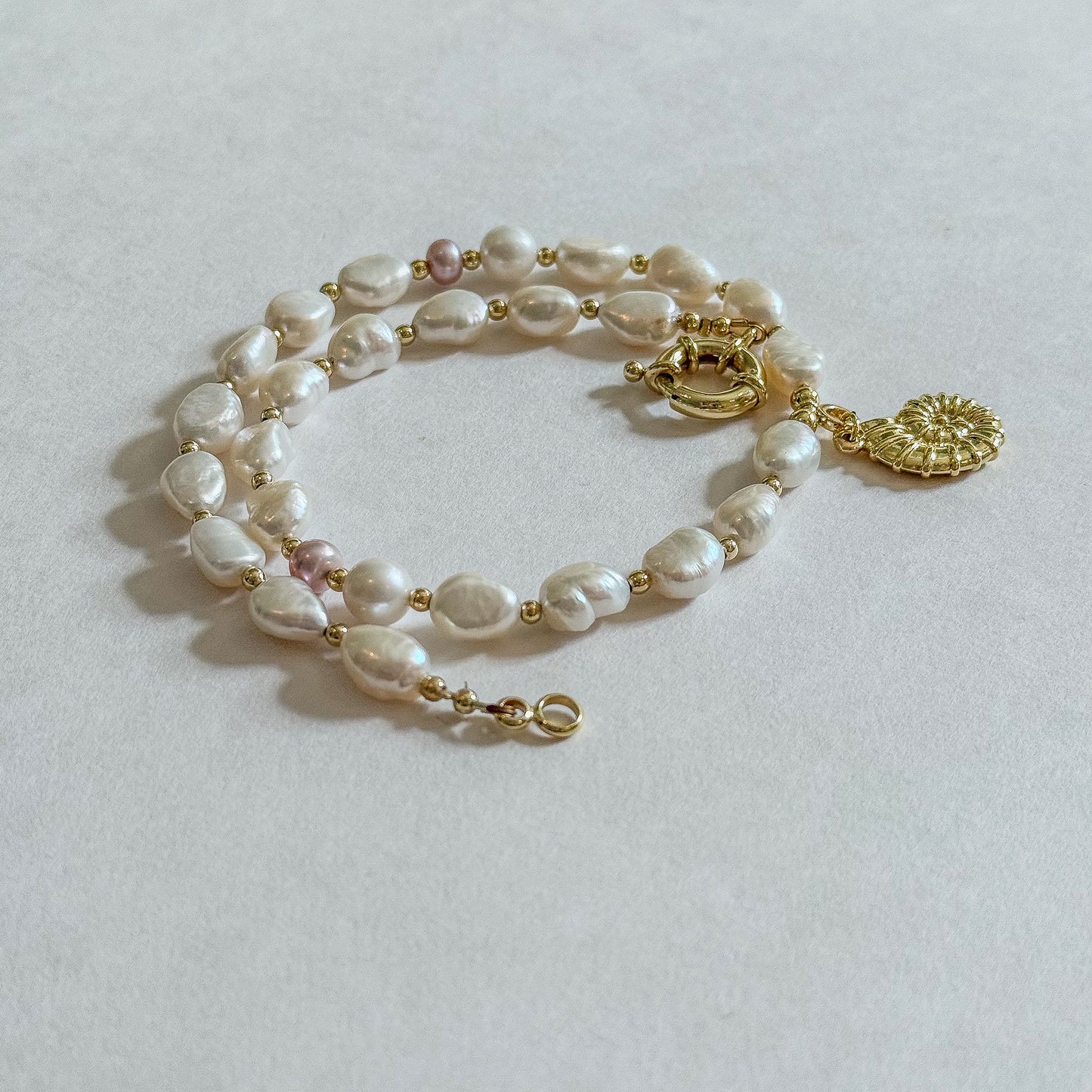 White baroque necklace with two pink round pearl accents, gold spring clasp, and gold shell charm by Hope and Raye