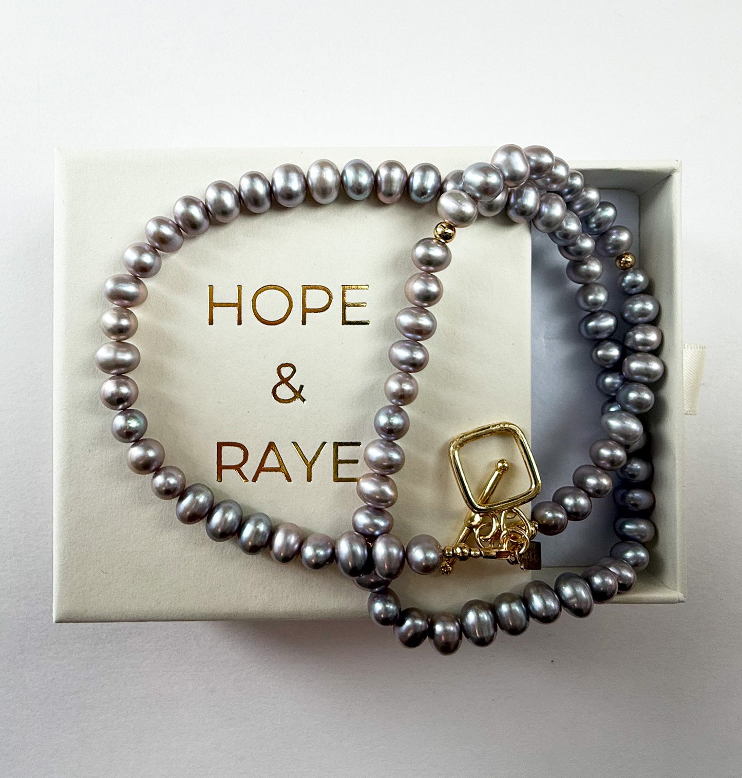Necklace with peacock freshwater pearls and gold toggle clasp displayed on Hope & Raye gift box