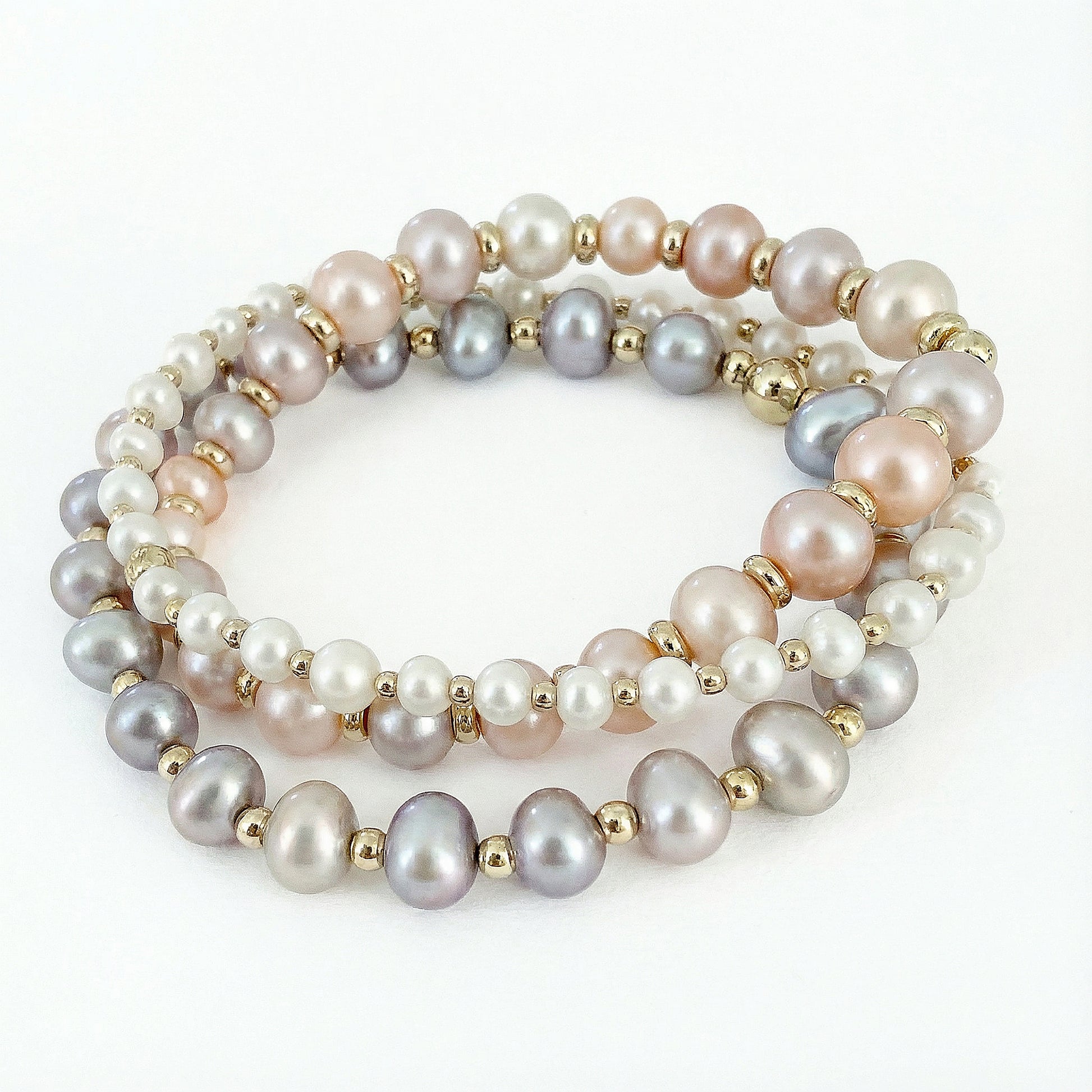 Pink, white, gray, and soft purple bracelet stack featuring three stretch bracelets made with natural freshwater pearls in varied sizes, finished with small gold-filled disc beads. Handcrafted pearl bracelet set by HOPE & RAYE.
